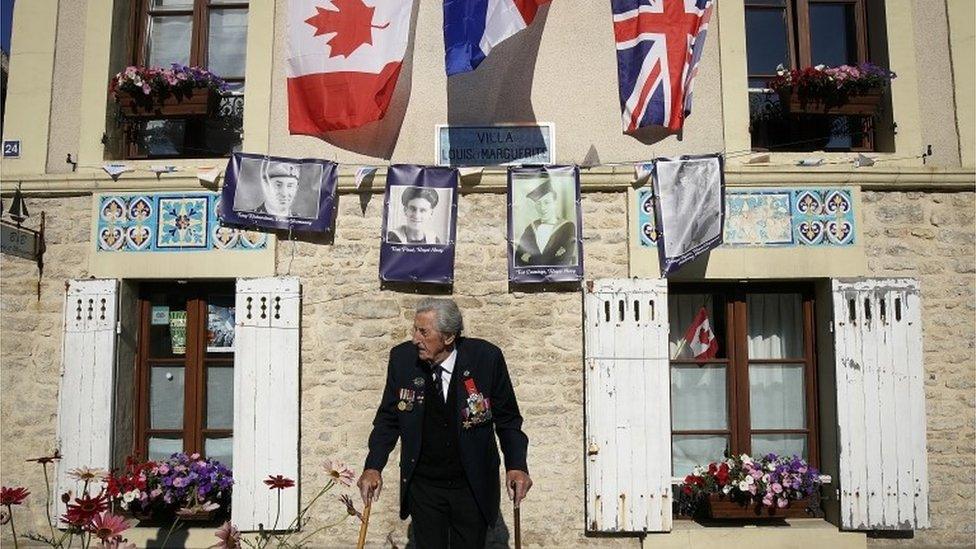 D-Day landing craft veteran, Ted Emmings, aged 94, of The Royal Navy, walks past a villa in Arromanches that has been decorated and is adorned with a photograph of him and other veterans