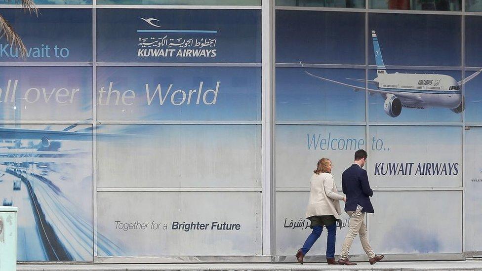 Customers walk past Kuwait Airways board in Kuwait