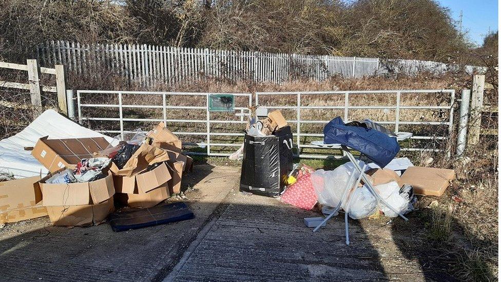 Mattress, cardboard boxes and other rubbish by a gate at the roadside