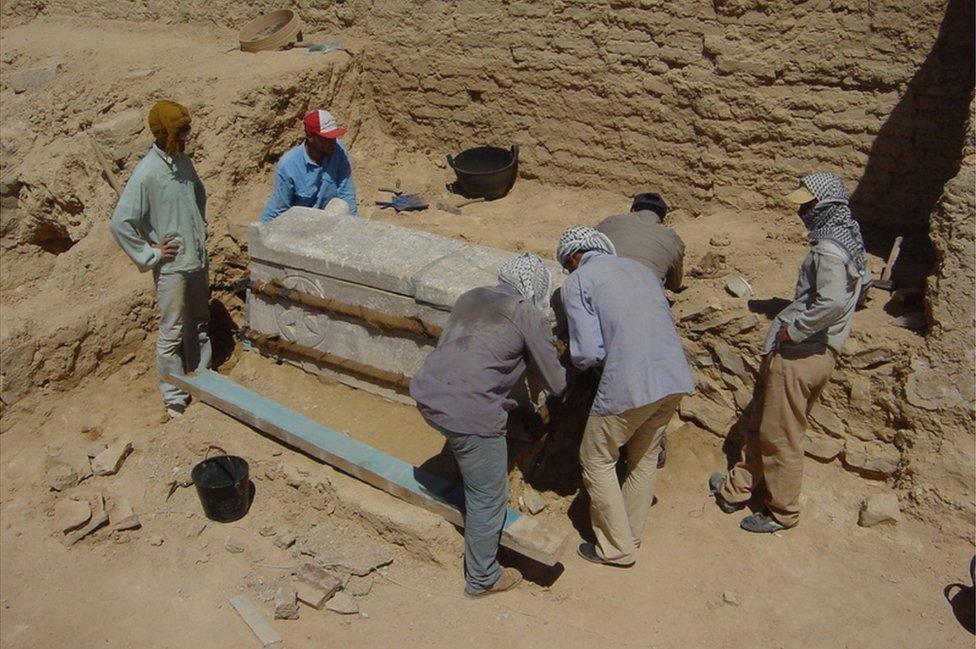 A team of men group around a stone tomb in the desert