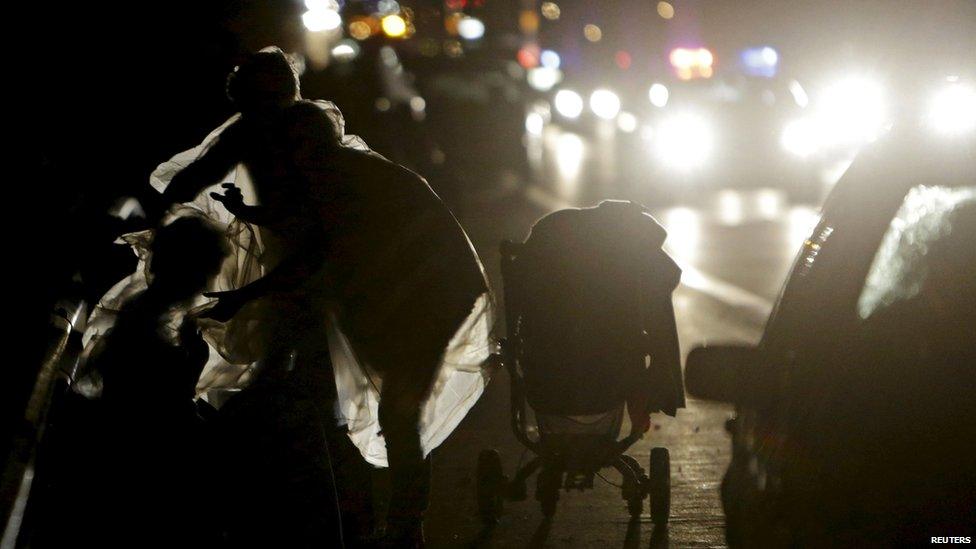 A migrants adjusts a plastic sheet in the rain