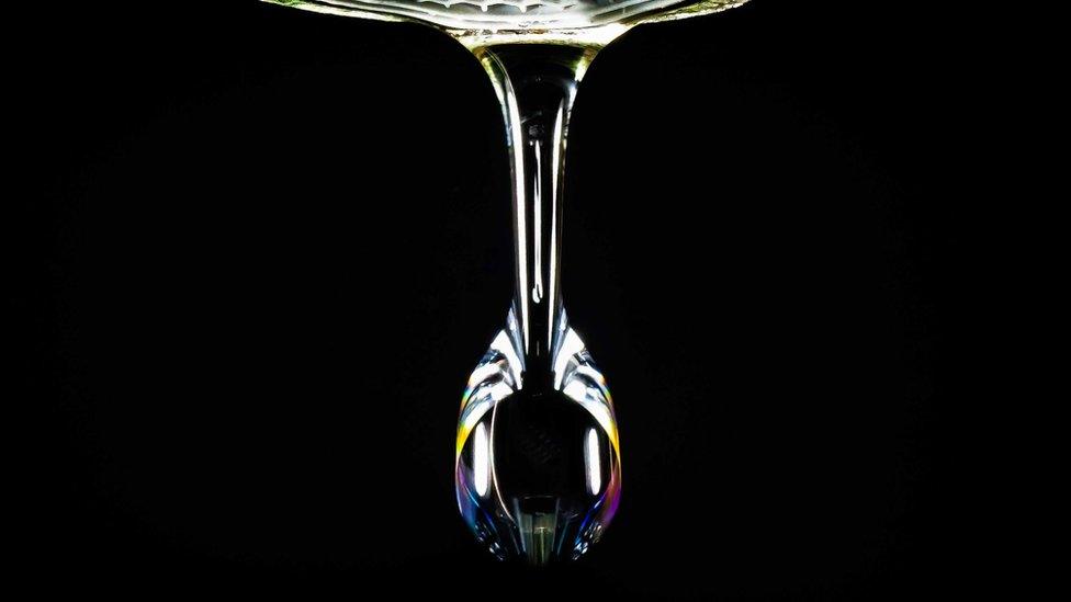 Close up of a water drop showing an array of rainbow colours against a black background