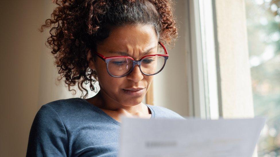 Woman looks concerned reading sheet of paper.