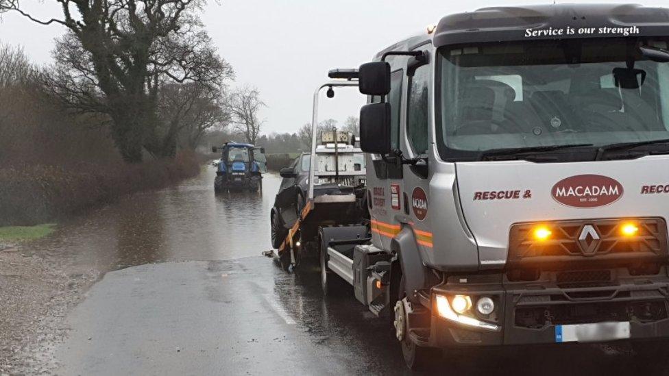 Tractor driving in flooded road and vehicle being towed by truck