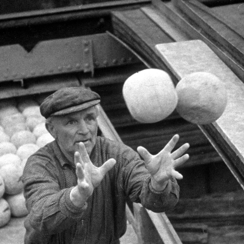 A workman catching two Edam cheeses as he loads them onto a barge for shipment to other parts of Holland (c1937)