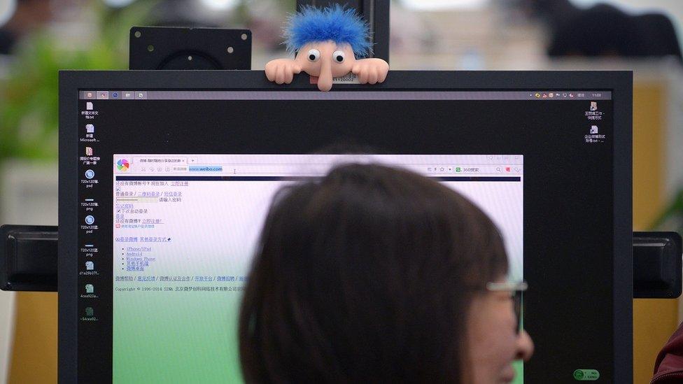 Long nosed troll hangs over a Chinese woman's computer monitor