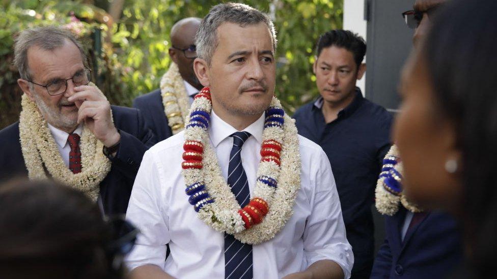 Gerald Darmanin wearing a white shirt and a white flower lei