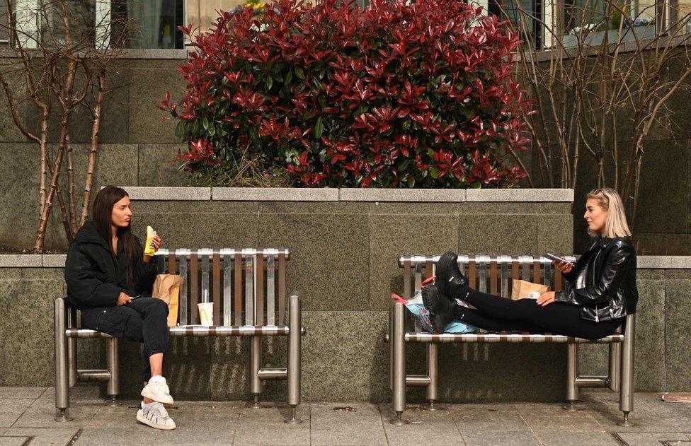 Two friends enjoy their lunch together at a safe distance in central Leeds on March 21, 2020, a day after the British government said it would help cover the wages of people hit by the coronavirus outbreak as it tightened restrictions to curb the spread of the disease.