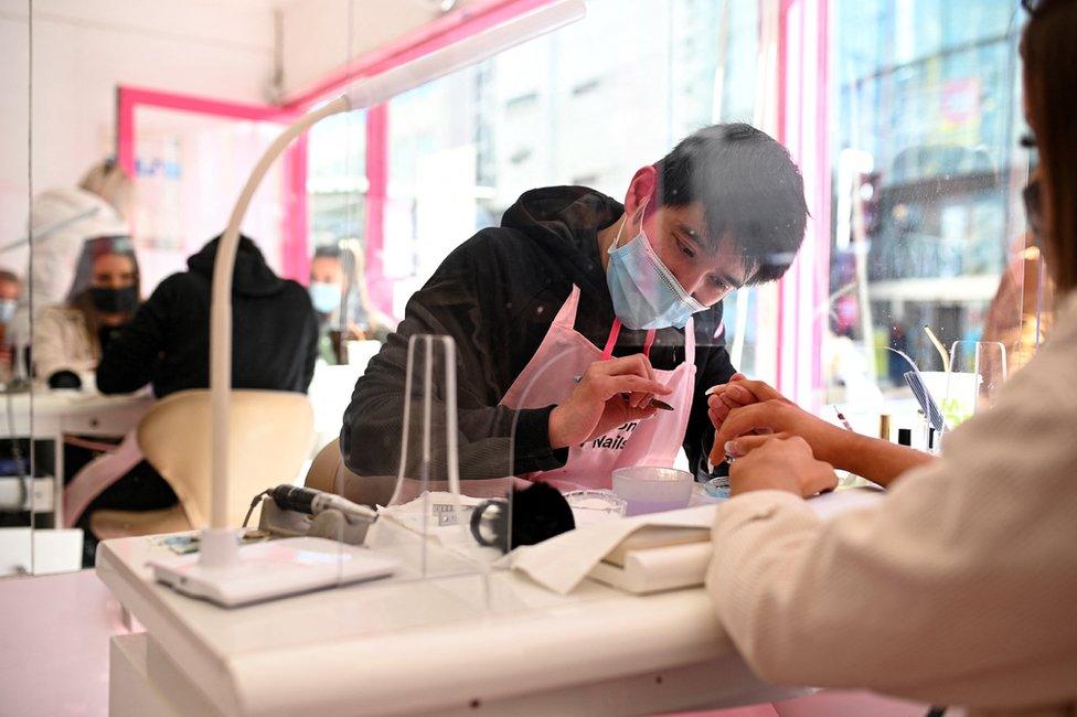 Customers sit in front of a protective screen as they have a manicure