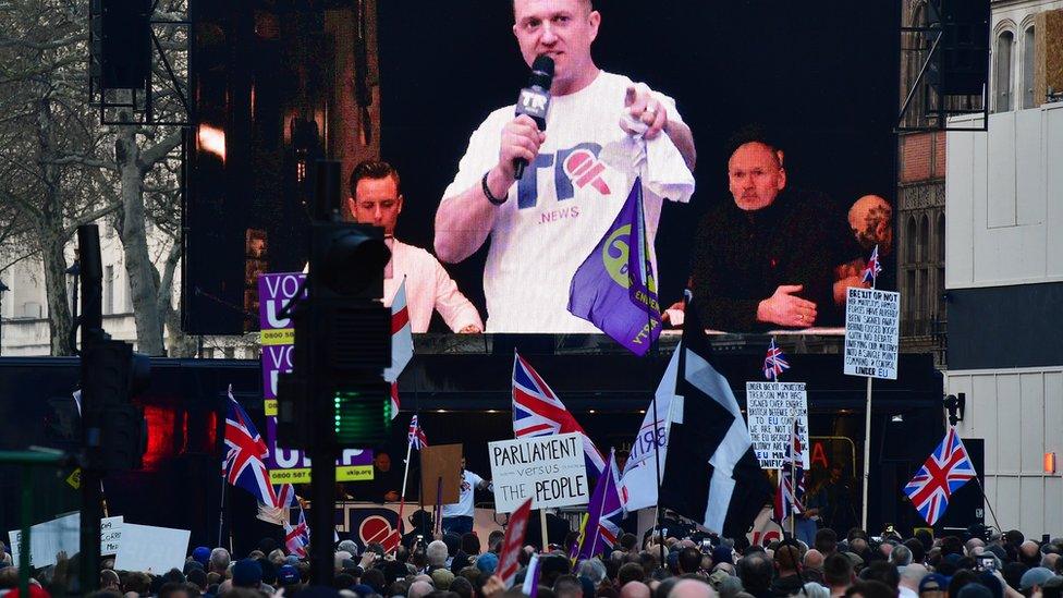 Far-right activist Tommy Robinson seem on a screen addressing protesters gathered outside the Houses of Parliament