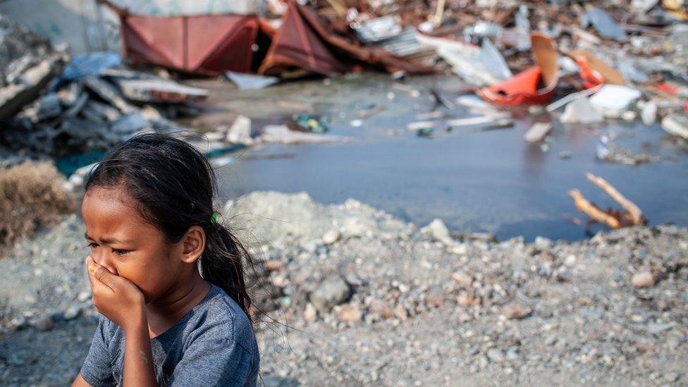 unknown child walking next to the ruins of a building that was destroyed by the earthquake