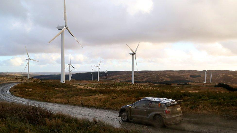 A car drives in front of wind turbines in Newtown, Powys