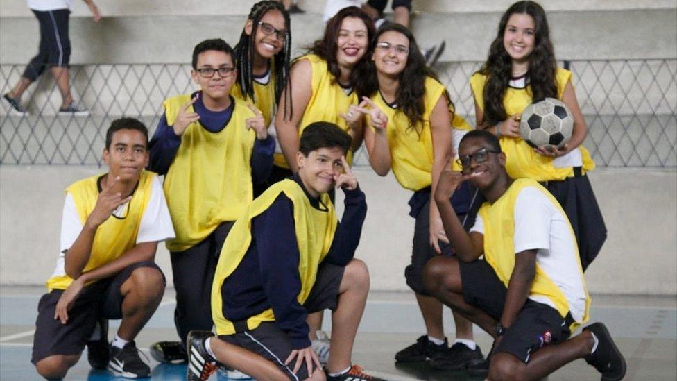 School kids in yellow sport bibs pose for the camera, and one girl holds a ball