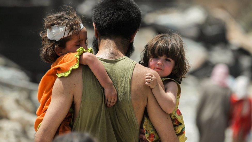 A man carries two young children as they flee fighting in the Old City of Mosul, Iraq (2 July 2017)