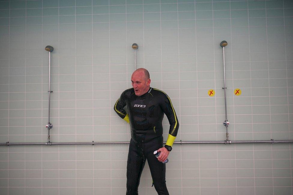 A man uses an outdoor shower whilst wearing a wet suit