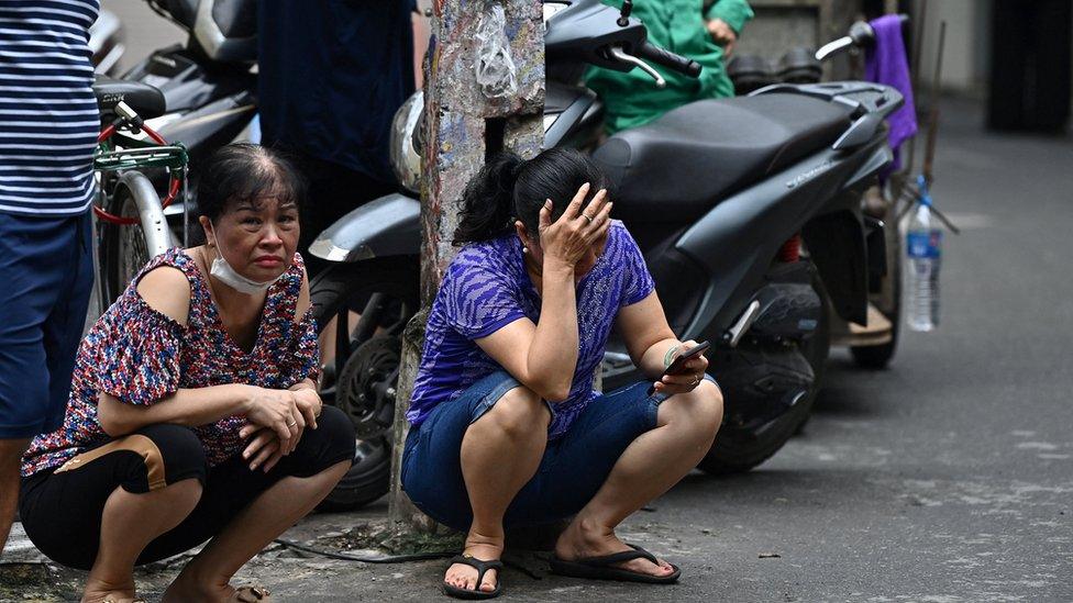 Women wait for information from relatives near the site of a major fire at an apartment block in Hanoi on September 13, 2023.