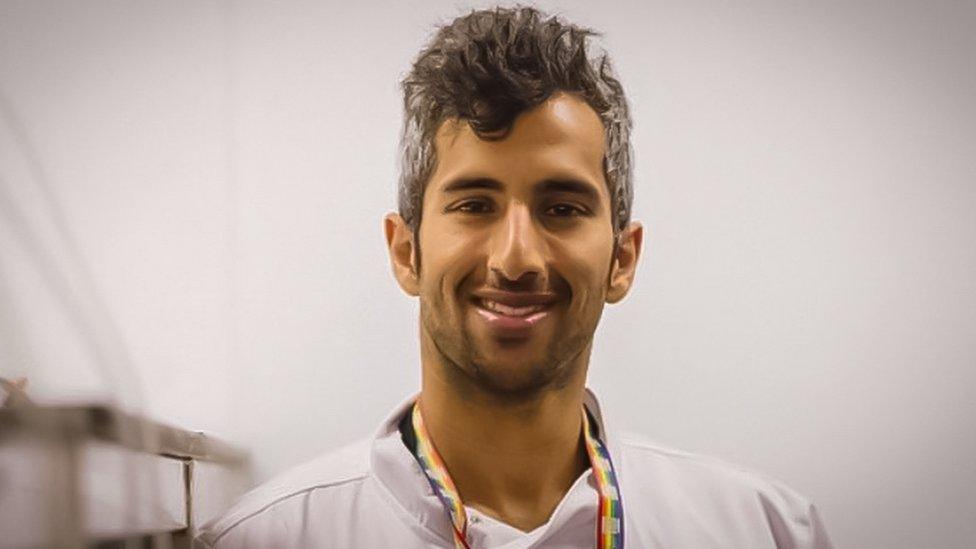 Numair Masud head and shoulder shot, smiling and wearing a rainbow flag lanyard