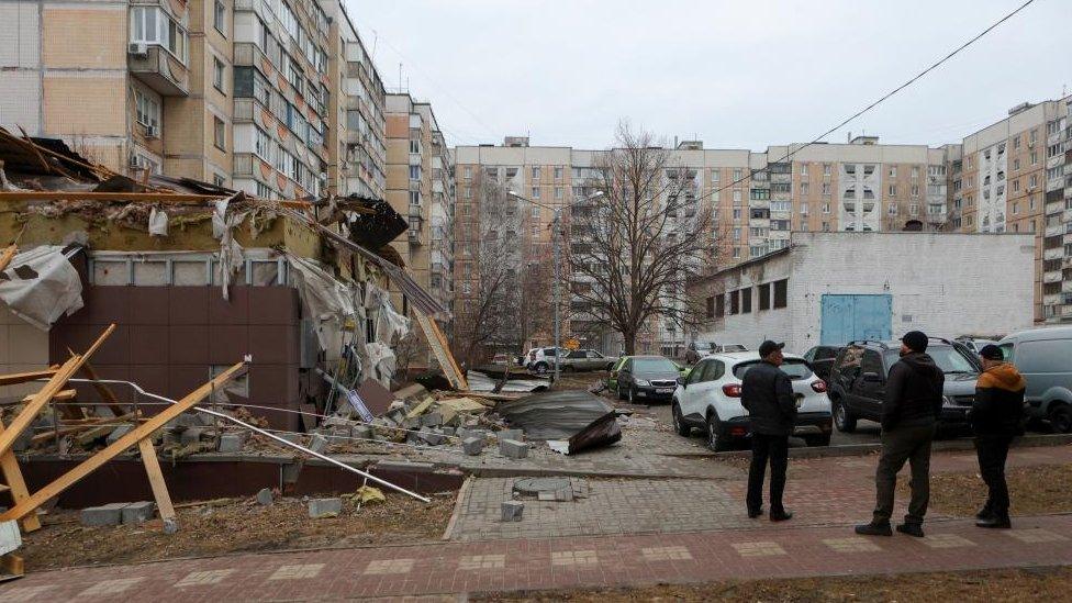 Three men stand next to a destroyed building hit by shelling in Belgorod