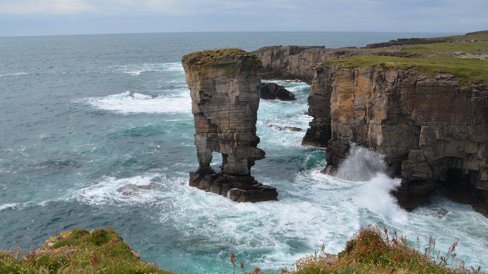 Yesnaby castle sea stack rock formation with white waves smashing against it with a grey looking sky