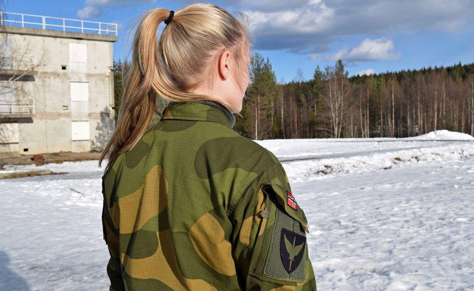 Venderla, 22, is seen from behind. She has a blonde ponytail and wears military fatigues