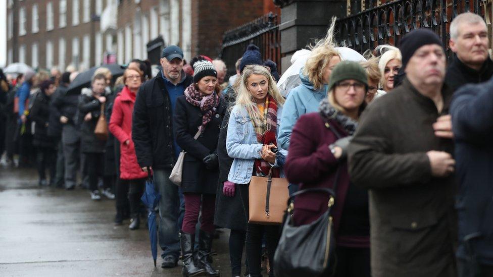 A queue stretches from the door of the Limerick church into the distance beyond the camera's frame.