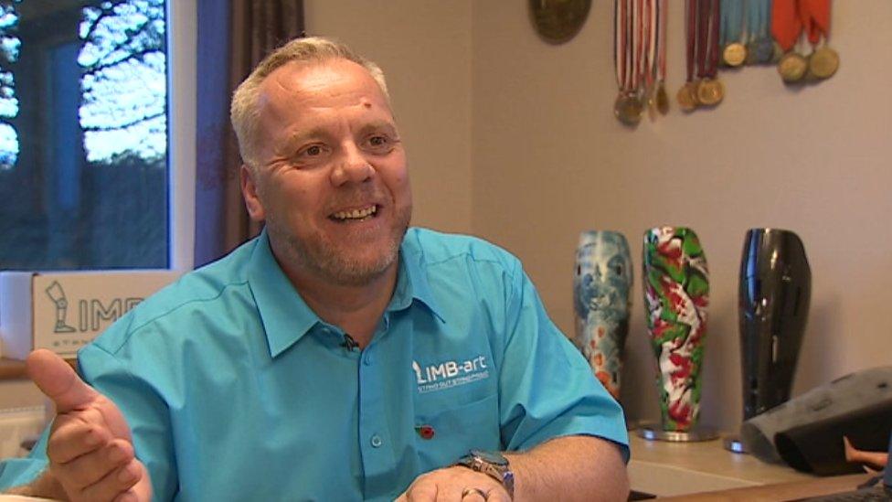 Mark Williams at home with three prosethetic legs and some medals in the background