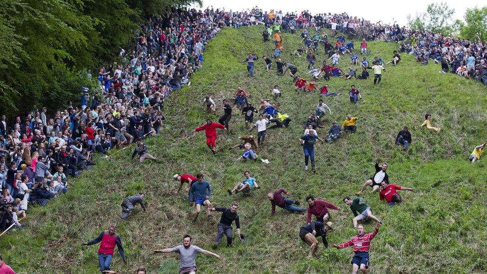 Crowds watch contestants running and falling down Coopers Hill as part of the cheese-rolling event