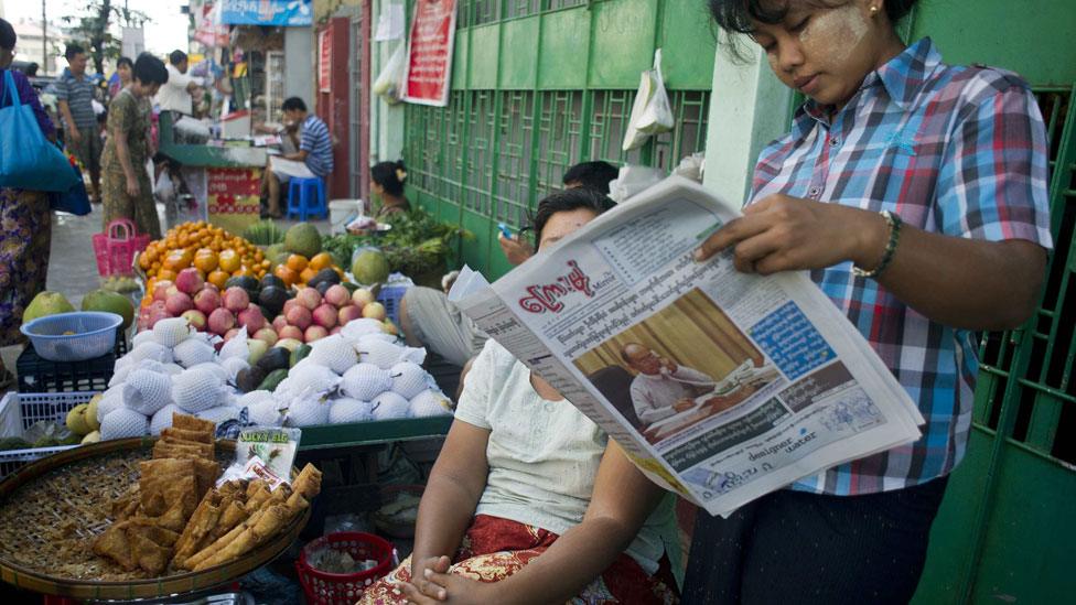 Vendors read a newspaper showing Myanmar President Thein Sein as they wait for customers at a street market in Yangon