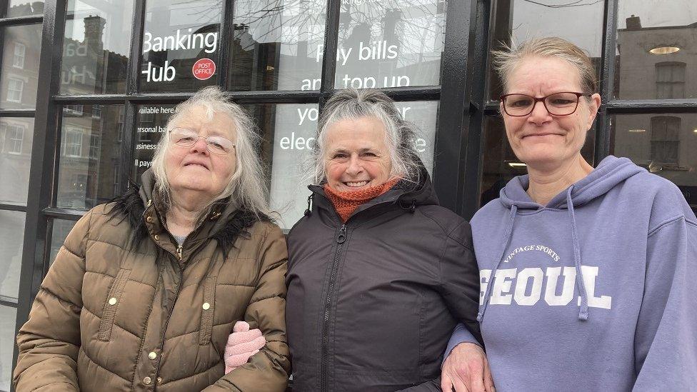 Three women stand in front of the new hub window in winter coats