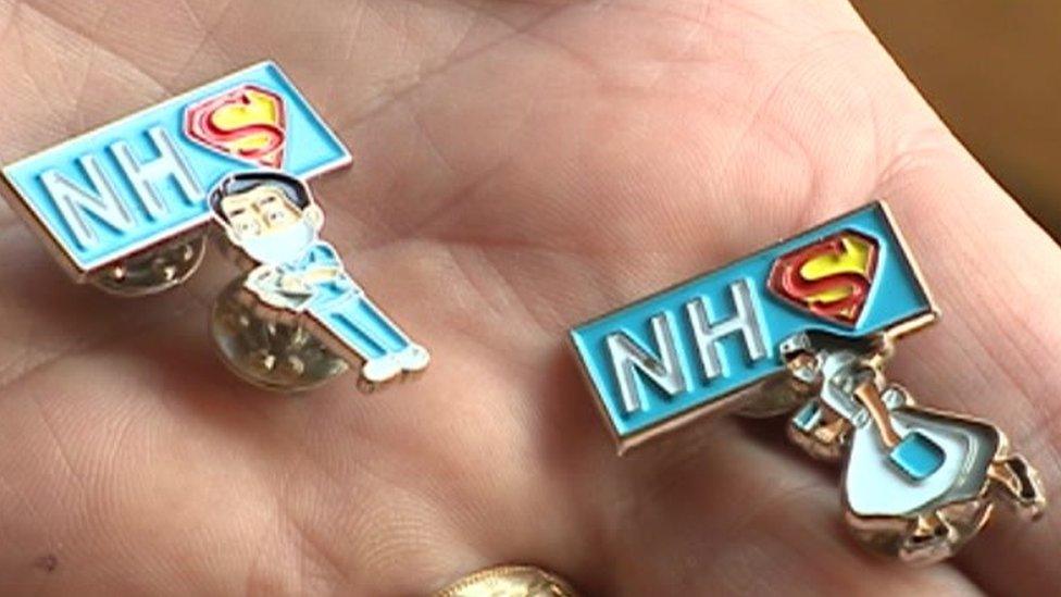 Badges in a hand with a nurse with a cape and a male nurse with a cape and NHS with the S in the Superman graphic