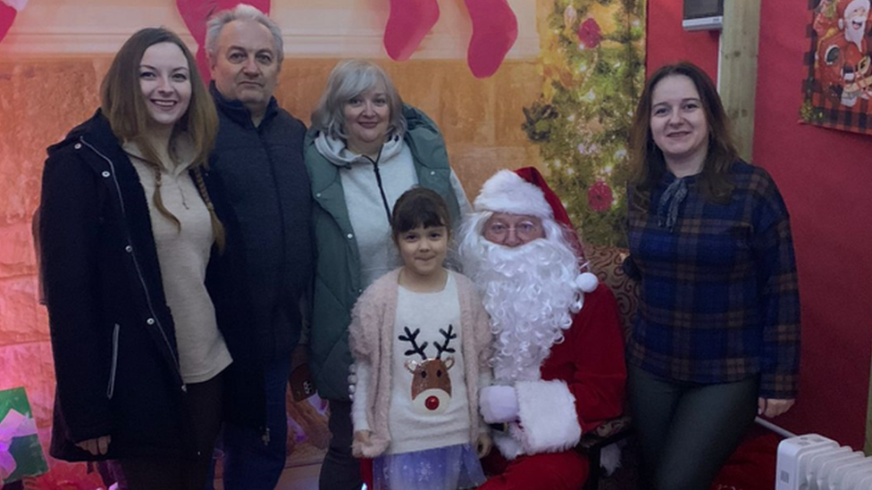 A little girl pictured with her mother, aunt, grandmother, grandfather and Santa