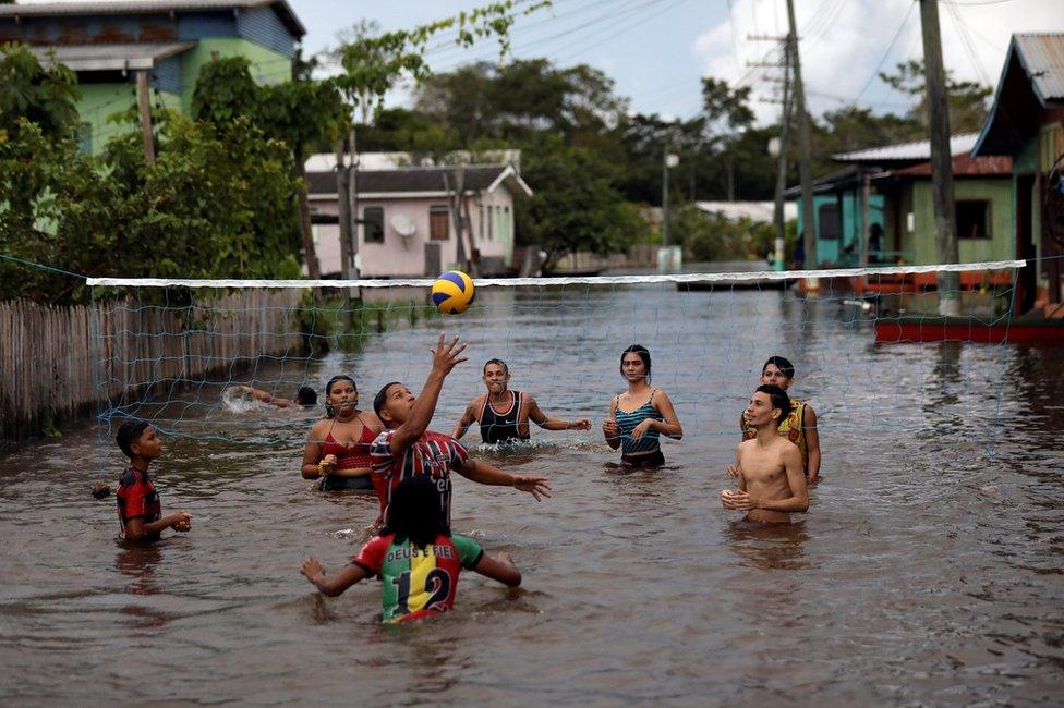 Residents play volleyball in a street flooded by the rising Solimoes river