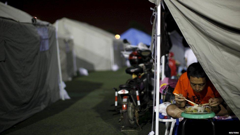 A man eats in a tent set up at a temporary shelter in a playground of a primary school, for people affected by explosions in Tianjin, China, on August 14, 2015