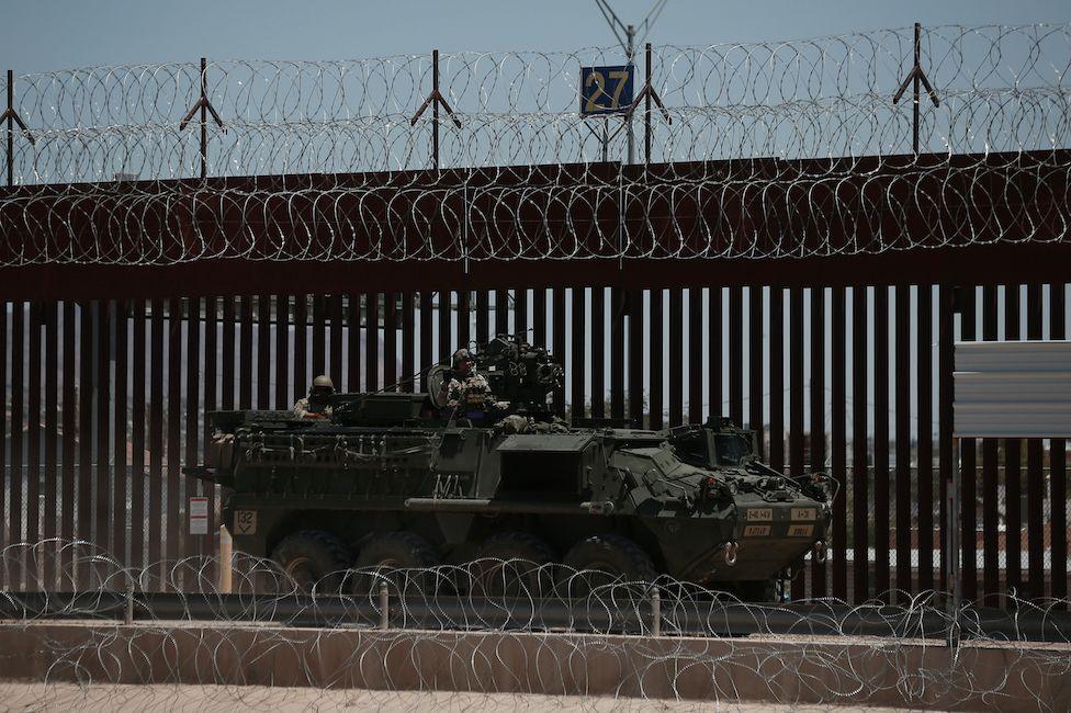 A US armored vehicle at border near El Paso with fence and barbed wire behind the tank.