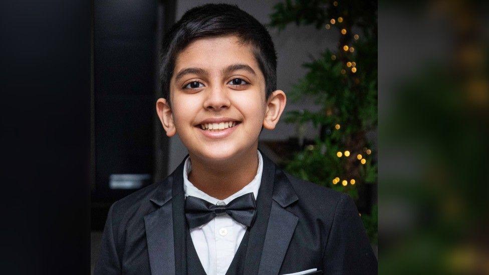 Arjun aged 11 smiling straight at the camera with dark hair and brown eyes, wearing a black tie suit. 