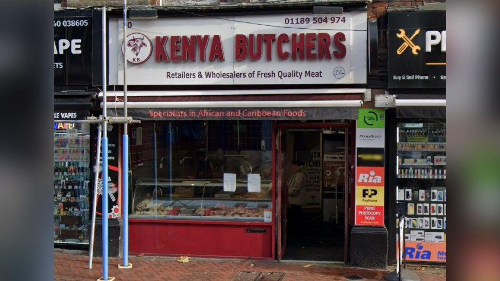 The shopfront of Kenya Butchers, which has a maroon shopfront with a large window.