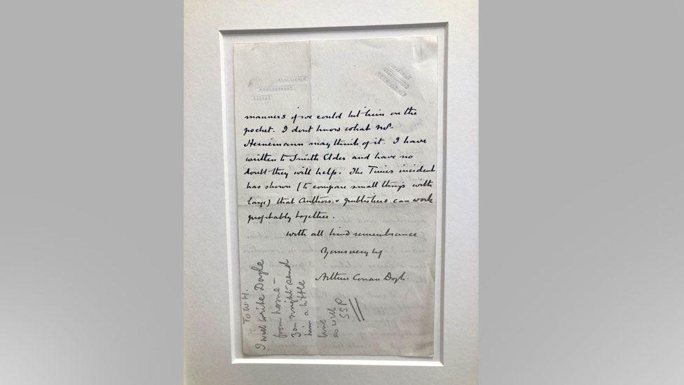 A framed handwritten letter from Sir Arthur Conan Doyle, written in black ink on white paper.