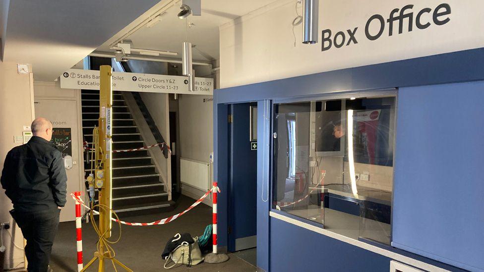 Interior of Oldham Coliseum theatre showing empty box office and foyer with red and white safety tape