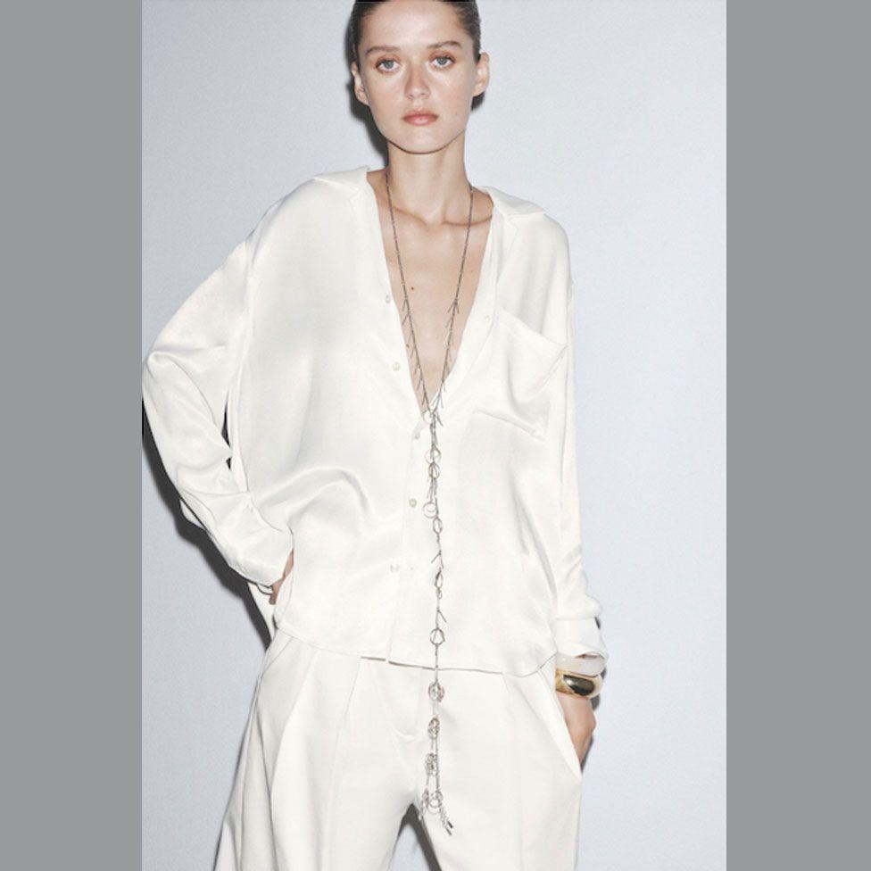 A pale model poses in a white Zara shirt staring at the camera with a blank expression and the low cut design of the top shows her protruding collarbones