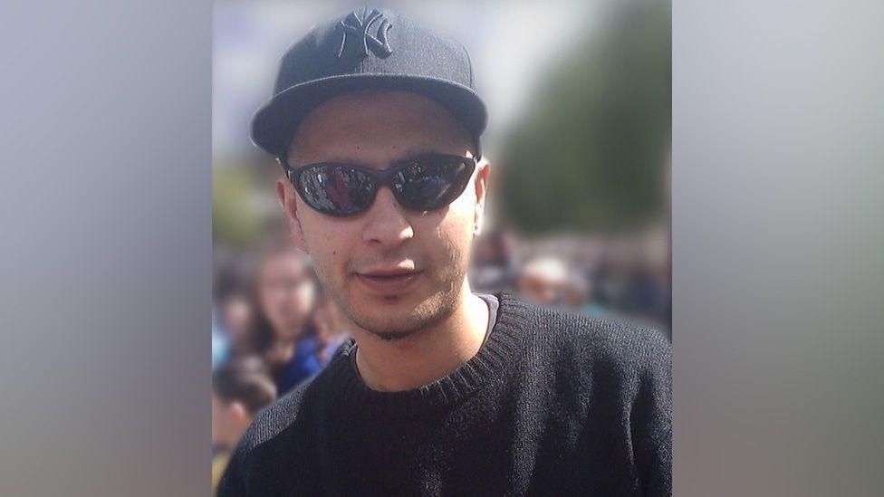 A photo of Omar Khan. He is wearing a black New York Yankees cap with black sunglasses and a black jumper. He is facing the camera and smiling.