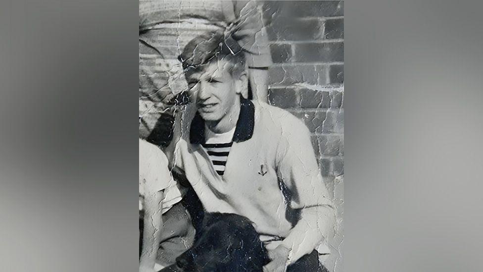 David Lawrence wearing a polo shirt in a black and white photo, sitting behind a dog