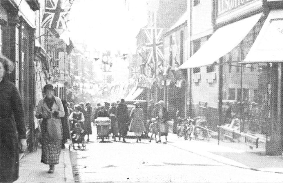 A black and white image of Friars Vennel with lots of people milling about and flags flying