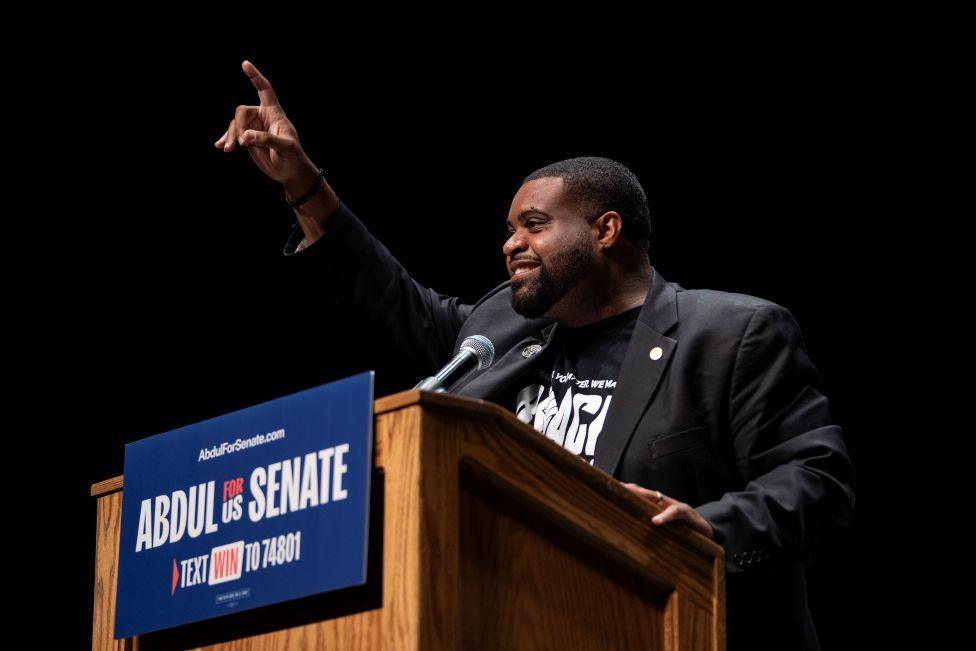 Donavan McKinney wearing a T-shirt and dark suit speaks from a podium at The People v The Powerful rally in Detroit in July