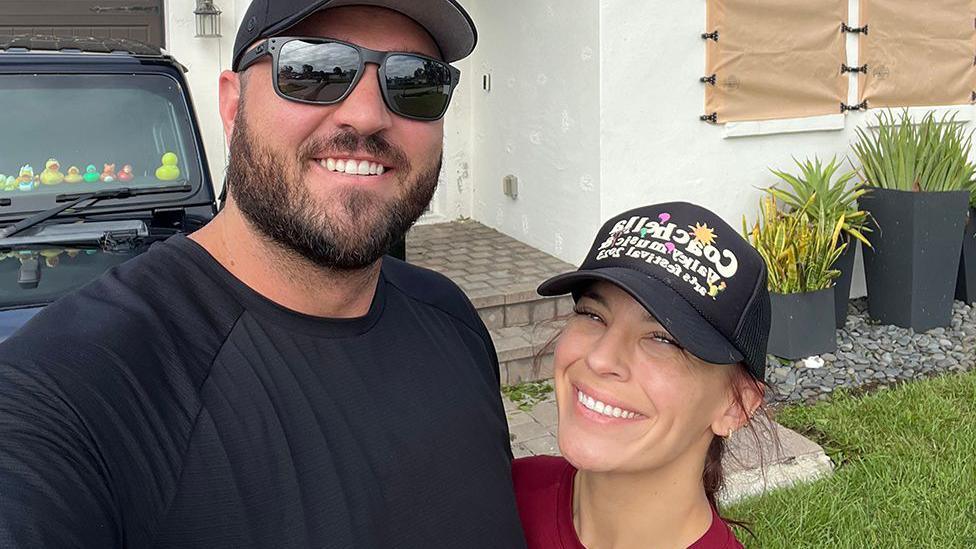 Sterling and Chynna Perkins, both wearing black caps, stand in front of a house