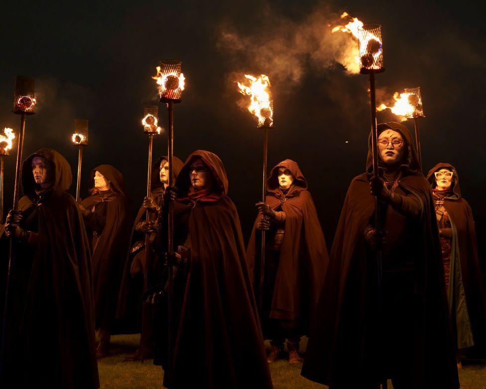 A group of people dressed in black cloaks and hoods, holding fire torches.