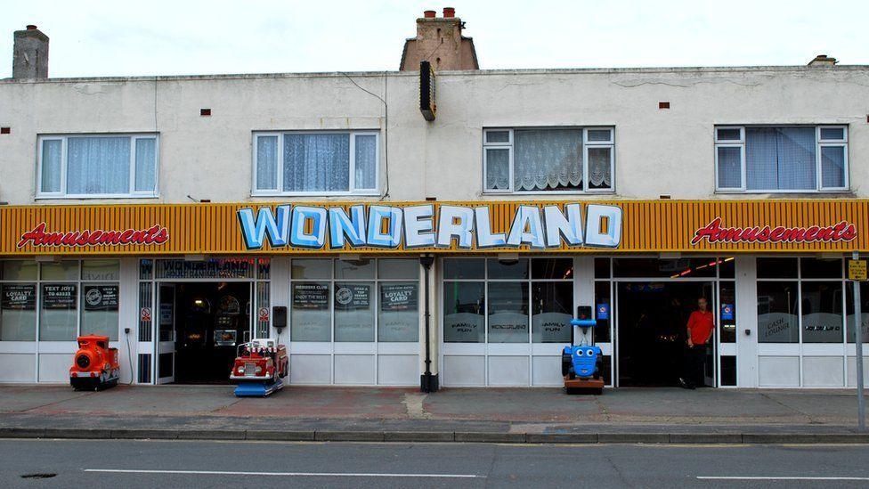 The entrance to Wonderland amusements in Jaywick. The bottom half of the building is dedicated to the amusements and has a yellow banner above the doors that reads "Wonderland". The top half of the building is occupied by flats.