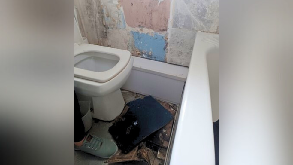 A bathroom in a state of disrepair with a hole in the floor 