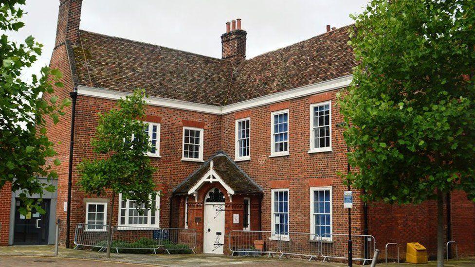 Cambridgeshire Coroner's Court  - a red-brick 18th Century looking building, with a porch in its middle. It is is two-storey and has white-framed windows. There are trees in leaf to its left and right