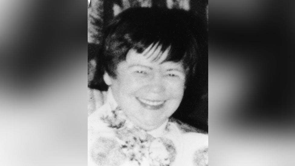 Mary McLaughlin in an old black and white photo, smiling broadly  with shiny black short hair and a floral dress.