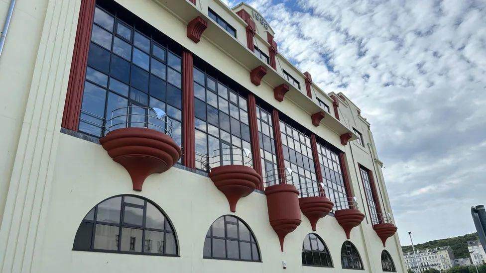 A large cream coloured building with red round balconies and large windows.